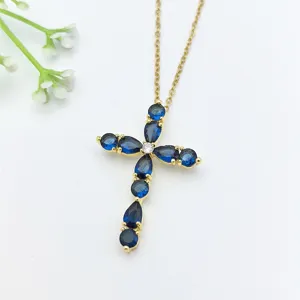 Dettaglio in primo piano di collana con croce placcata in oro con zirconi blu e trasparenti.