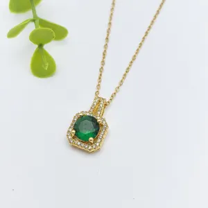 Primo piano di una collana con ciondolo a alone dorato e uno zircone verde centrale luminoso.