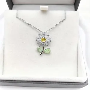 Vista ravvicinata di una collana con ciondolo a fiore in argento, zirconi brillanti e foglie verdi.