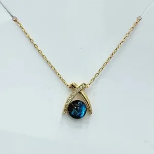 Primo piano della collana con ciondolo a croce dorata con perla blu scintillante cielo stellato.