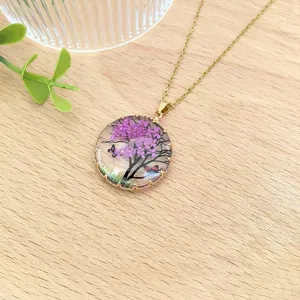 Primo piano di una collana con ciondolo in resina e fiori secchi su legno, vintage.