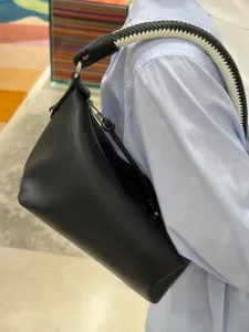 Detail view of a black leather shoulder bag featuring a stylish black and white woven strap.