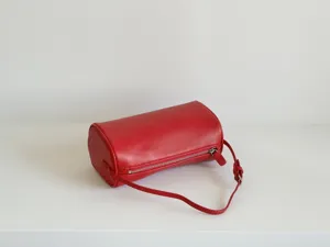 Détail de sac cylindrique en cuir rouge avec coutures fines, fermeture éclair et quincaillerie.