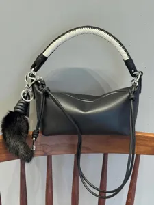 Black leather shoulder bag with white woven handle and plush charm detail for women.