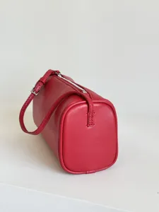Gros plan détaillé du sac cylindrique en cuir rouge minimaliste avec texture fine et fermeture éclair.