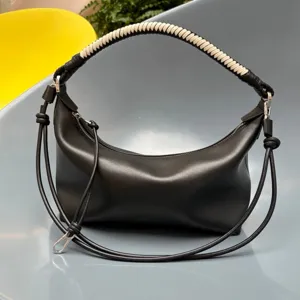 Detail view of black leather dumpling shoulder bag with woven handle and sleek metal strap.