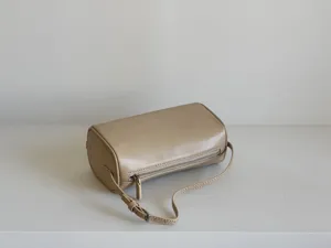 Sac cylindrique minimaliste en cuir beige, sac bandoulière tendance style 90s léger chic.