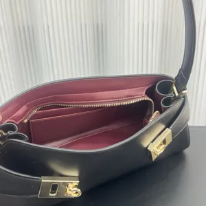 Detailed view of black leather shoulder underarm bag with burgundy interior and gold hardware.
