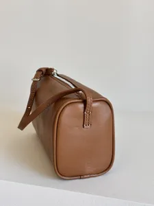 Gros plan sur les details du sac cylindrique en cuir marron avec texture et fermeture eclair.
