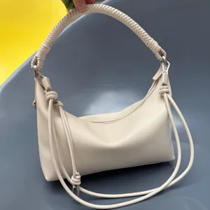 Beige leather shoulder bag with braided top handle and knotted side cords for women fashion.