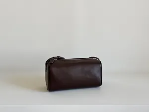 Détail d'un sac cylindrique en cuir marron foncé avec texture fine et fermeture éclair.