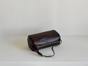 Sac cylindrique en cuir marron foncé en détail, montrant la texture lisse et la fermeture éclair.