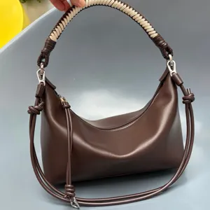 Brown leather shoulder bag, detail view featuring woven top handle and knotted strap design.