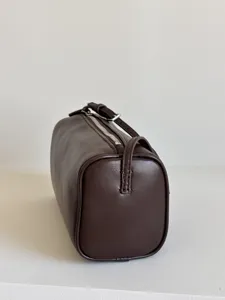 Détail de sac tonneau en cuir marron foncé, texture de sac cylindrique minimaliste années 90.
