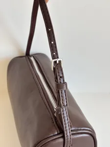 Vue détaillée du sac porté épaule cylindrique minimaliste en cuir marron avec fermeture.