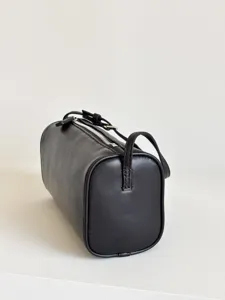 Vue détaillée du sac bandoulière cylindrique minimaliste en cuir marron foncé avec fermeture éclair.