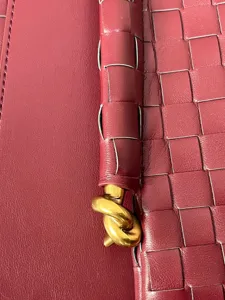 Close-up of premium burgundy woven leather handbag with signature knot hardware detail.