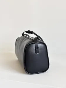 Détail d'un sac cylindrique minimaliste en cuir noir, montrant la fermeture et la sangle.