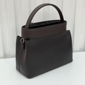 Leather handbag detail view showing dark brown structured top handle design and fine texture.