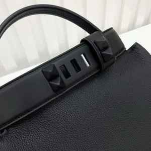 Black leather handbag detail shot featuring pyramid studs, top handle, and metal hardware.