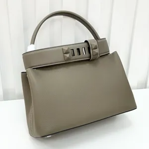 Luxury taupe leather top handle handbag with iconic metal pyramid studs and elegant flap.