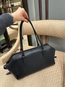 Close-up detail shot of a black genuine leather East-West bowling bag held by hand.