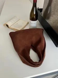 Détail de sac porté épaule hobo en daim marron, poignée découpée triangulaire et texture douce.