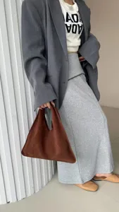 Vue de détail d'un élégant sac à main triangulaire en daim marron avec un blazer gris.