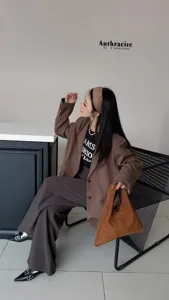 Vue détaillée d'une femme élégante en blazer marron avec sac en suédine dans un décor moderne.