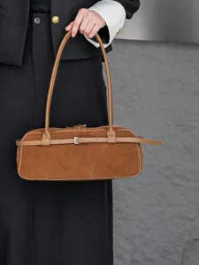 Close-up of retro brown suede shoulder baguette bag showcasing a chic wrap-around belt buckle.