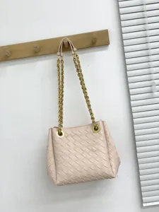 Détail de sac seau en cuir tressé rose avec bandoulière chaîne dorée et œillets.