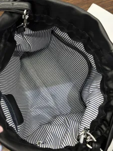 Black leather bucket bag interior detail showing blue striped lining and zipper pocket.