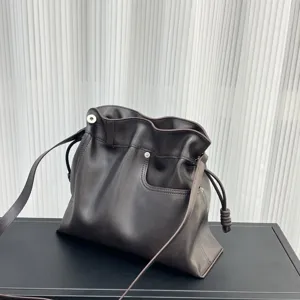 Vista detallada de un bolso cubo de cuero suave marrón oscuro con elegantes nudos laterales.