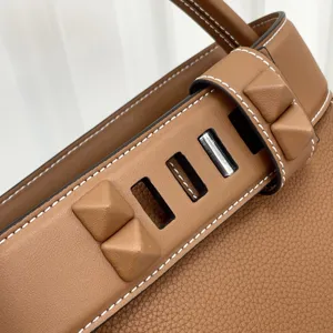 Close-up detail shot of luxury leather handbag with pyramid studs and contrast stitching.