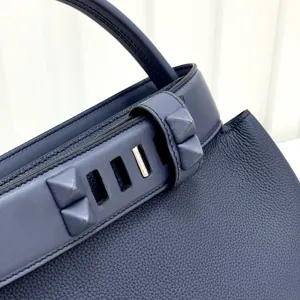 Detailed view of luxury blue leather handbag with pyramid stud strap and metal lock closure.