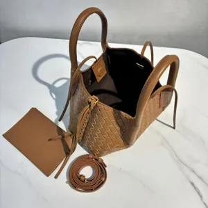 Detail shot of brown leather woven tote bag with handle, strap and matching pouch on marble.