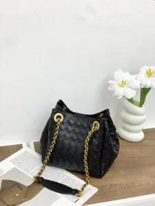 Vue détaillée du sac seau en cuir noir tressé à la main avec bandoulière à chaîne dorée.