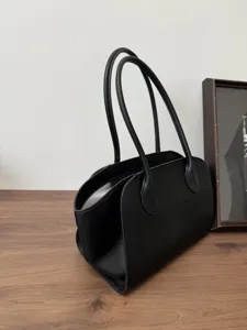 Close-up detail of a minimalist black leather tote handbag, featuring structured dual top handles.