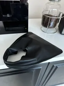 Vue de détail du sac à main triangle en cuir noir, montrant un design de pli asymétrique.