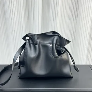 Primer plano del bolso saco de piel suave negra con nudos laterales delicados y detalles finos.