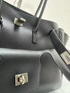 Black leather handbag detail close-up showcasing metal turn-lock hardware and fine stitching.