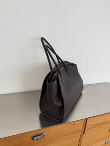 Detailed view of the dark brown leather tote bag with slim dual handles and large capacity.