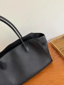 Detailed view of minimal black leather tote bag, showing pebble texture and thin shoulder strap.