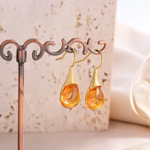 Close-up of elegant teardrop gemstone earrings with gold hooks and orange stones on a stand.