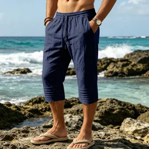 Close-up view of men's casual navy blue cropped shorts with drawstring and pleated hems on beach.