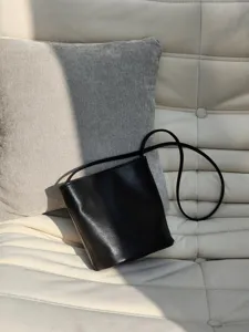 Vue détaillée d'un sac seau minimaliste en cuir noir posé sur un fauteuil clair.