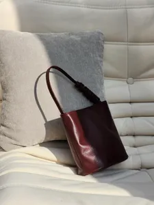 Détail du sac seau en cuir bordeaux, design minimaliste avec bandoulière froncée.