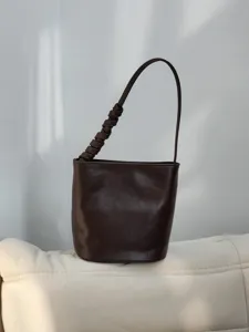 Sac seau en cuir marron foncé détail montrant une lanière plissée et design épuré.