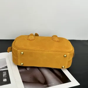 Detailansicht der gelben Wildleder-Bowlingtasche mit goldenen Bodenstiften und Griffen.