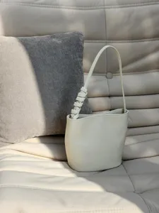 Vue rapprochée d'un sac seau minimaliste en cuir beige avec poignée nouée sur fond intérieur.